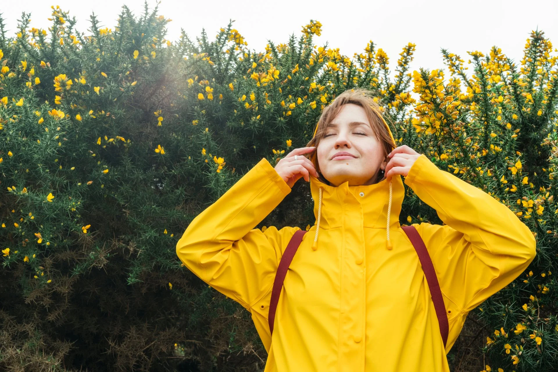 Woman in yellow raincoat pulls hood off her head because the sun is shining now.