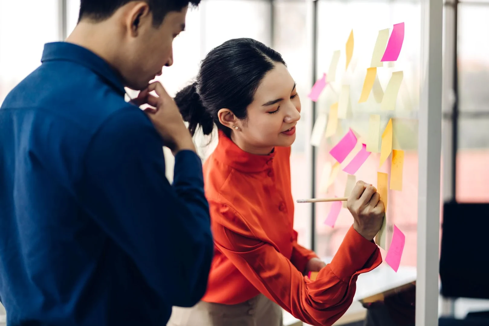 Eine Wissenschaftlerin und ein Wissenschaftler arbeiten hinter einer Glasfassade und mischen Chemikalien mit Großgeräten.