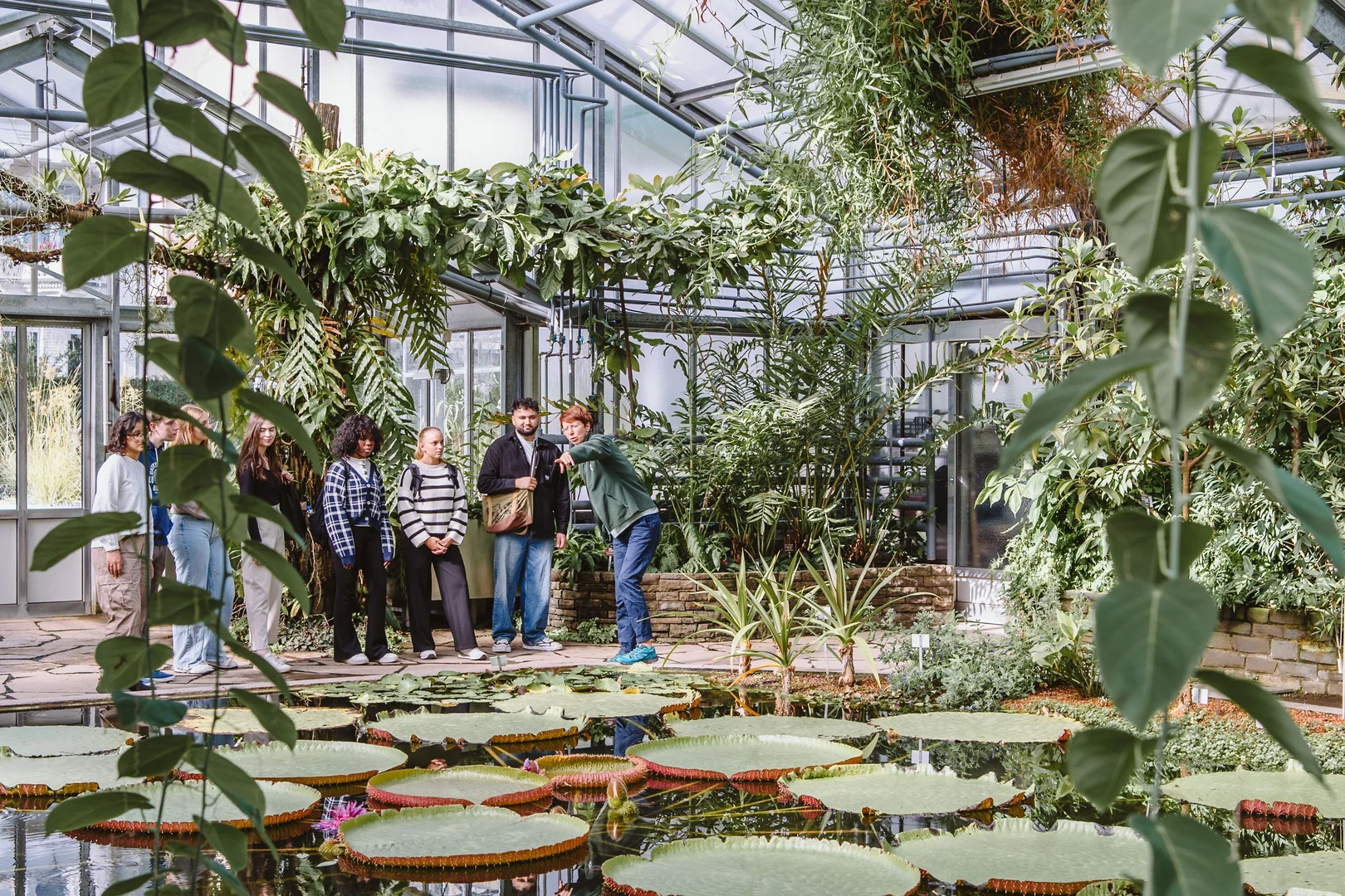 Eine Wissenschaftlerin und ein Wissenschaftler arbeiten hinter einer Glasfassade und mischen Chemikalien mit Großgeräten.