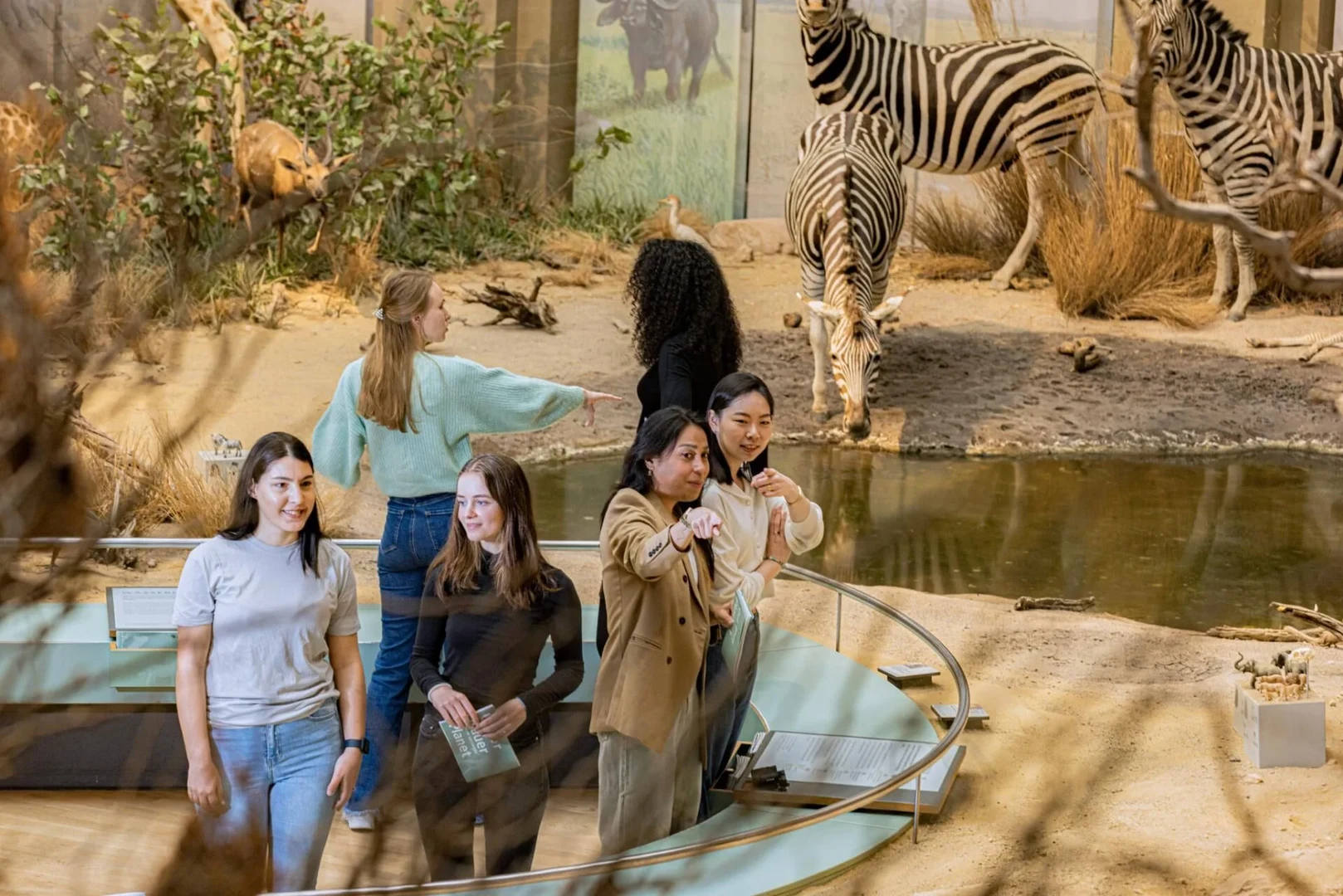 Eine Wissenschaftlerin und ein Wissenschaftler arbeiten hinter einer Glasfassade und mischen Chemikalien mit Großgeräten.