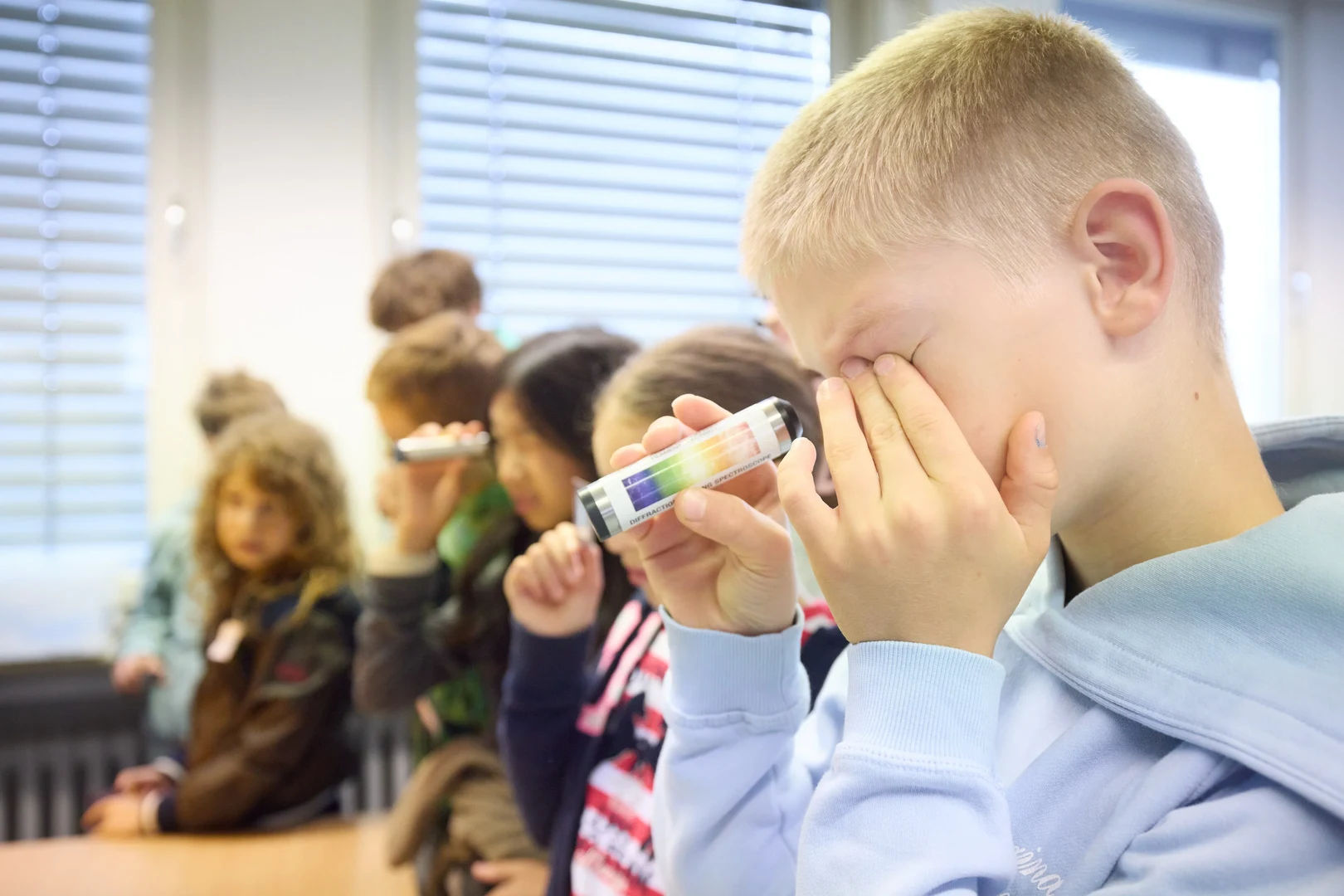 Mithilfe von kleinen Röhren betrachten die Kinder das Licht unterschiedlicher Gasentladungen.