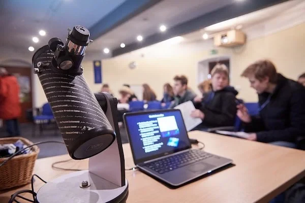 Ein Teleskop und ein Laptop im Institut für Astronomie, dahinter eine Gruppe Schüler*innen.