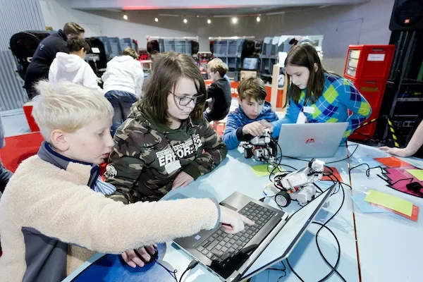 Schüler*innen sitzen an einem Tisch und arbeiten an Laptops und Minirobotern.