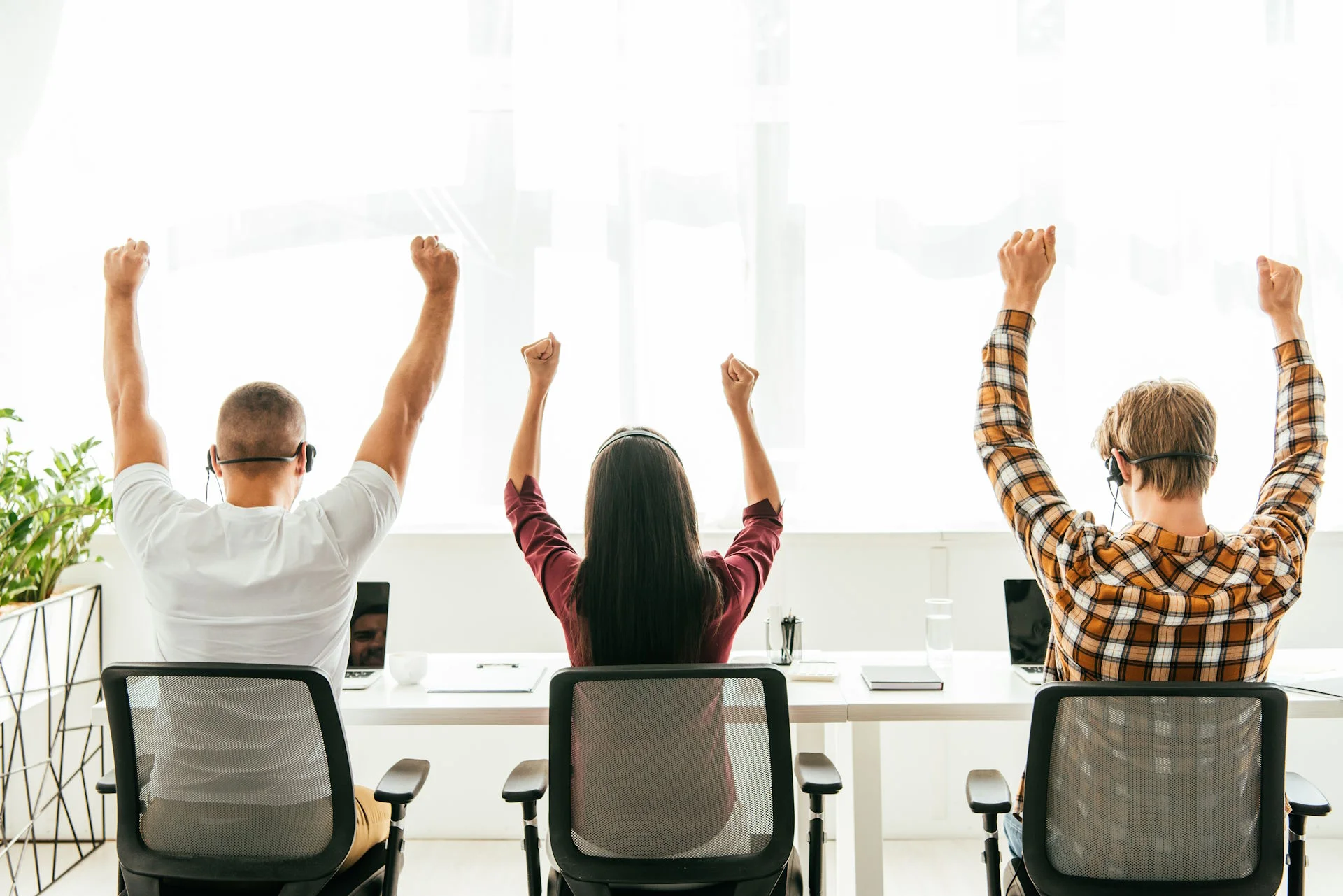 Drei Personen sitzen mit dem Rücken zur Kamera und strecken sich am Abeitsplatz