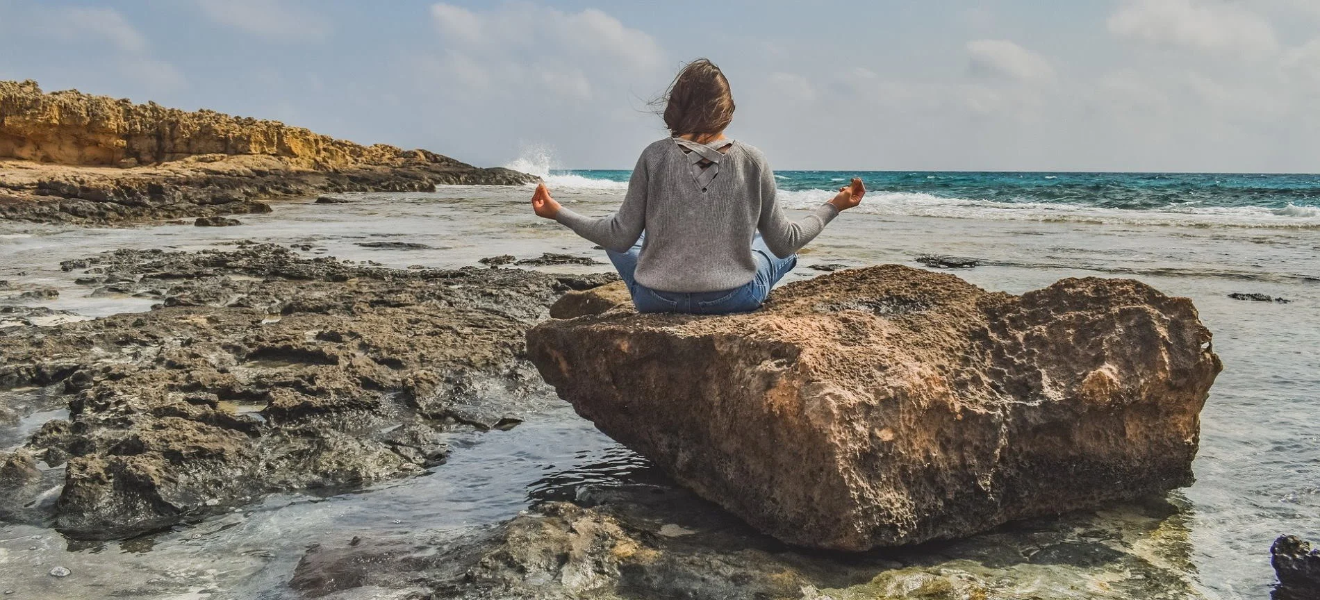 Frau meditiert auf einem Felsen am Strand