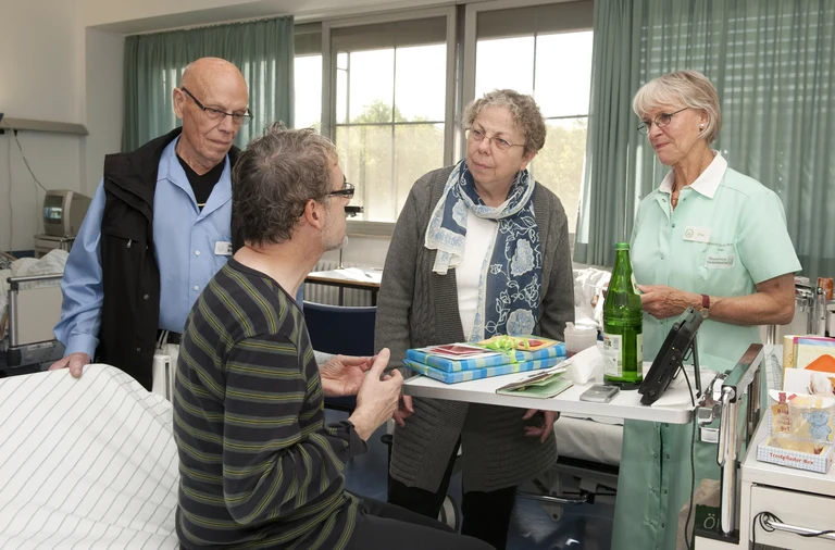 Grüne Damen und Grüner Herr im Gespräch mit einem Patienten (vorne):