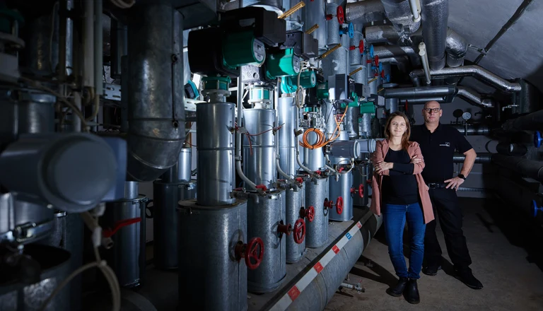 Annika Veith und Techniker Jörg Radzey aus dem Energieteam vor einer Heizungsanlage.