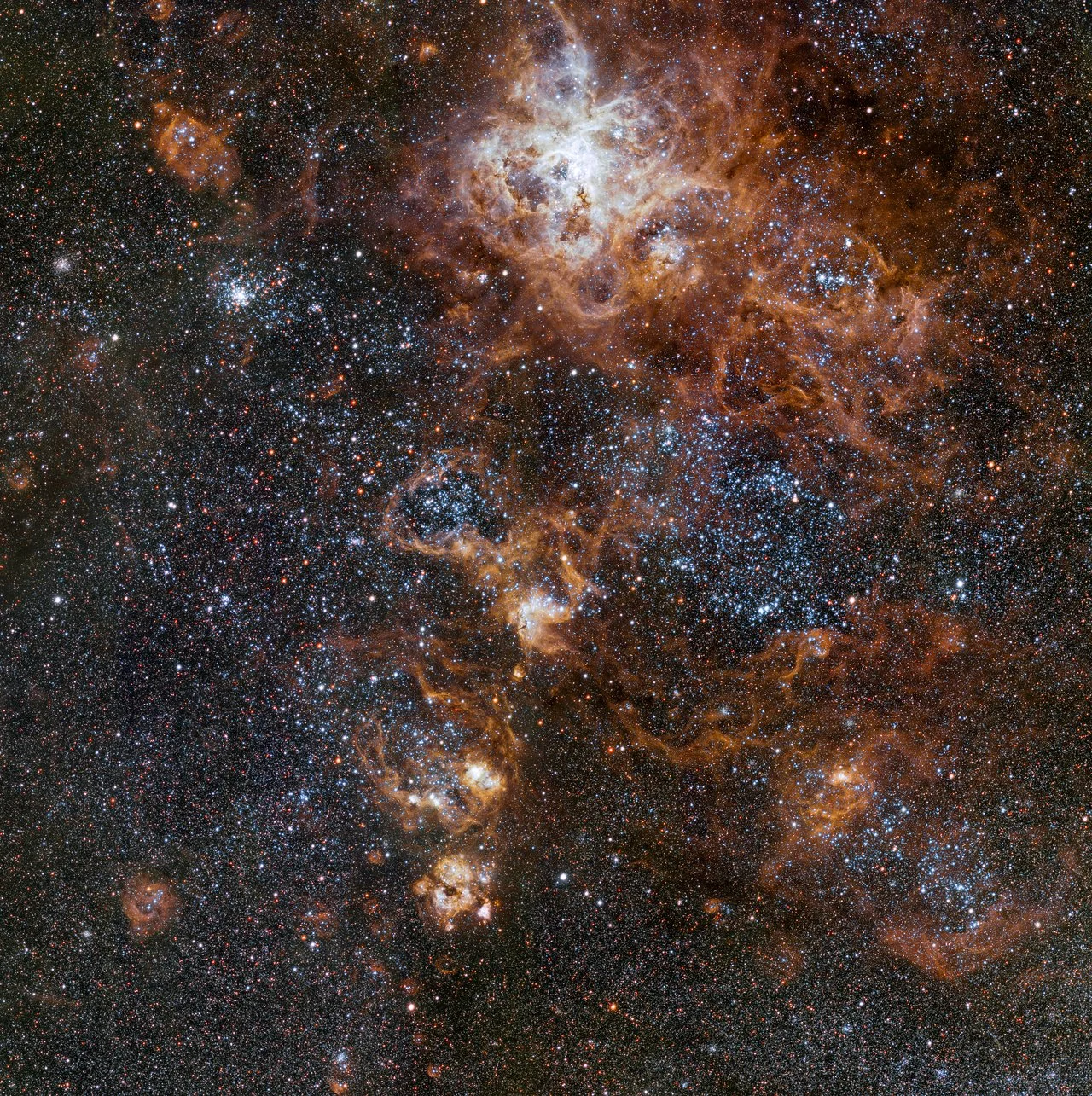 Glowing brightly about 160 000 light-years away, the Tarantula Nebula is the most spectacular feature of the Large Magellanic Cloud, a satellite galaxy to our Milky Way. This image from VLT Survey Telescope at ESO’s Paranal Observatory in Chile shows the region and its rich surroundings in great detail. It reveals a cosmic landscape of star clusters, glowing gas clouds and the scattered remains of supernova explosions.