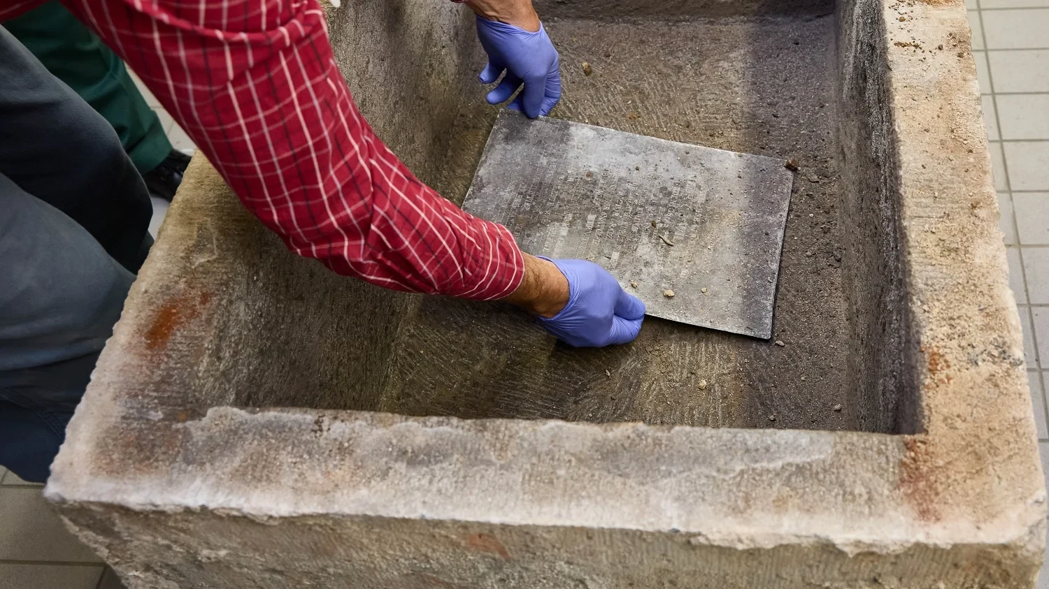 Archaeologists carefully remove the lead plate from the opened foundation stone in order to examine and document the find.