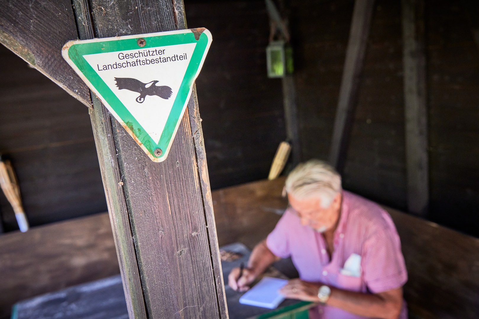 Prof. Dr. Wolfgang Böhme recording notes in his little wooden house. A sign saying “Protected Landscape Element” provides some  indication of the biodiversity value of his garden. Photo: Volker Lannert